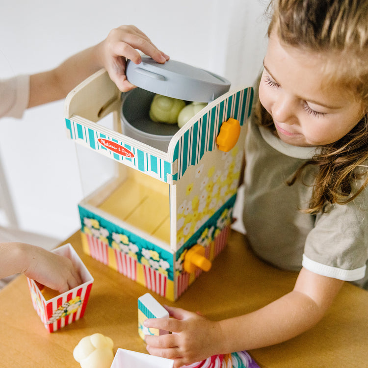 A kid playing with The Melissa & Doug Fun at the Fair! Wooden Popcorn Popping Play Food Set