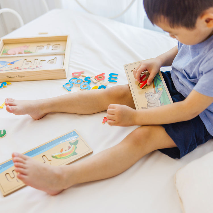 A kid playing with The Melissa & Doug See & Spell Wooden Educational Toy With 8 Double-Sided Spelling Boards and 64 Letters