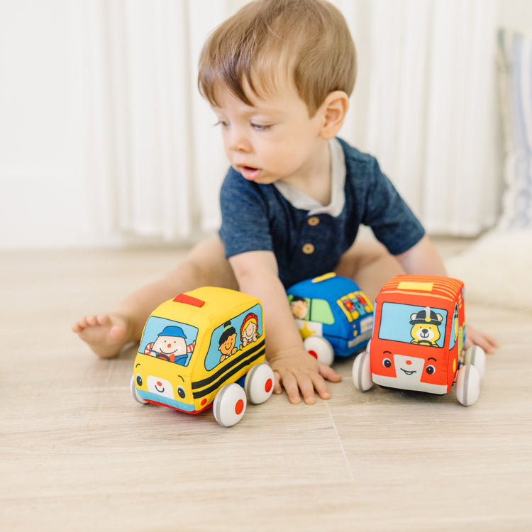 A kid playing with The Melissa & Doug K's Kids Pull-Back Vehicle Set - Soft Baby Toy Set With 4 Cars and Trucks and Carrying Case