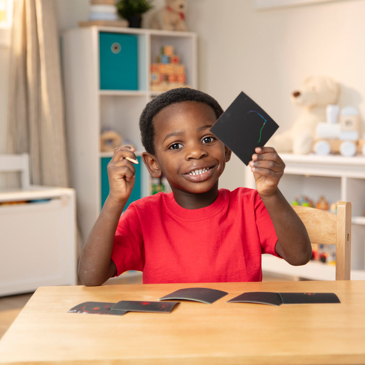 A kid playing with The Melissa & Doug Scratch Art Rainbow Mini Notes (125) With Wooden Stylus