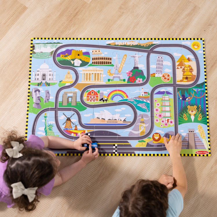 A kid playing with The Melissa & Doug Race Around the World Tracks Cardboard Jigsaw Floor Puzzle and Wind-Up Vehicles – 48 Pieces, for Boys and Girls 3+