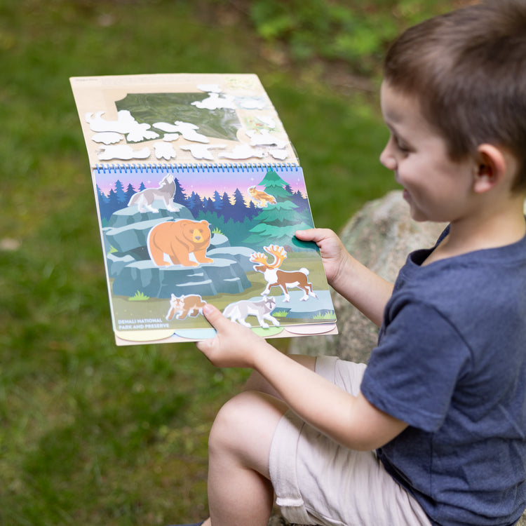 A kid playing with The Melissa & Doug National Parks Reusable Stickers Jumbo Pad: Park Animals - 5 Scenes, 121 Puffy and Cling Stickers