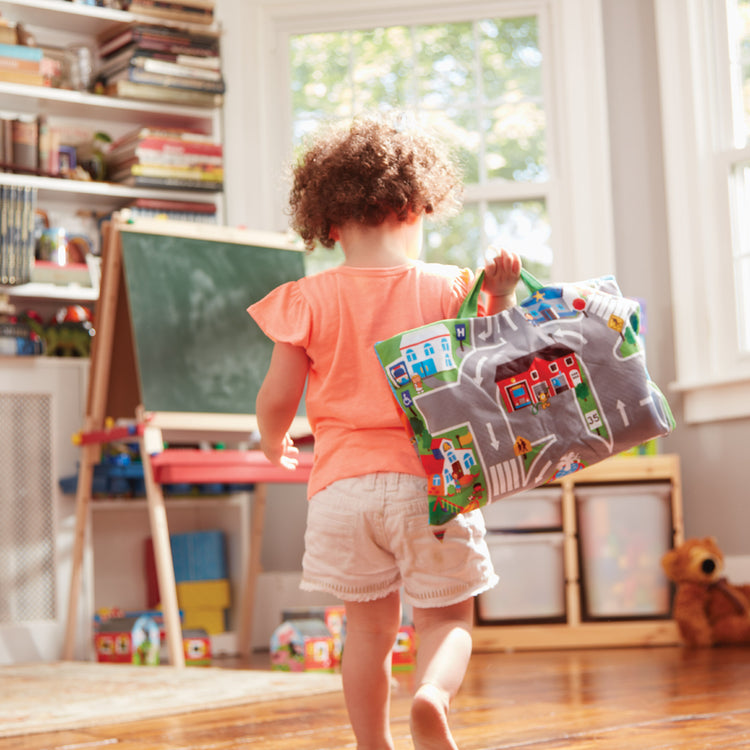 A kid playing with The Melissa & Doug Take-Along Town Play Mat (19.25 x 14.25 inches) With 9 Soft Vehicles