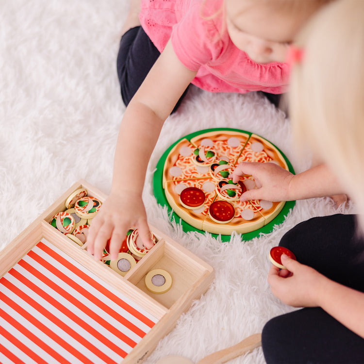 A kid playing with The Melissa & Doug Wooden Pizza Party Play Food Set With 36 Toppings