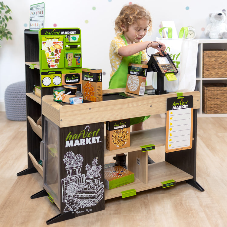 A kid playing with The Melissa & Doug Harvest Market Grocery Store and Companion Collection Accessories