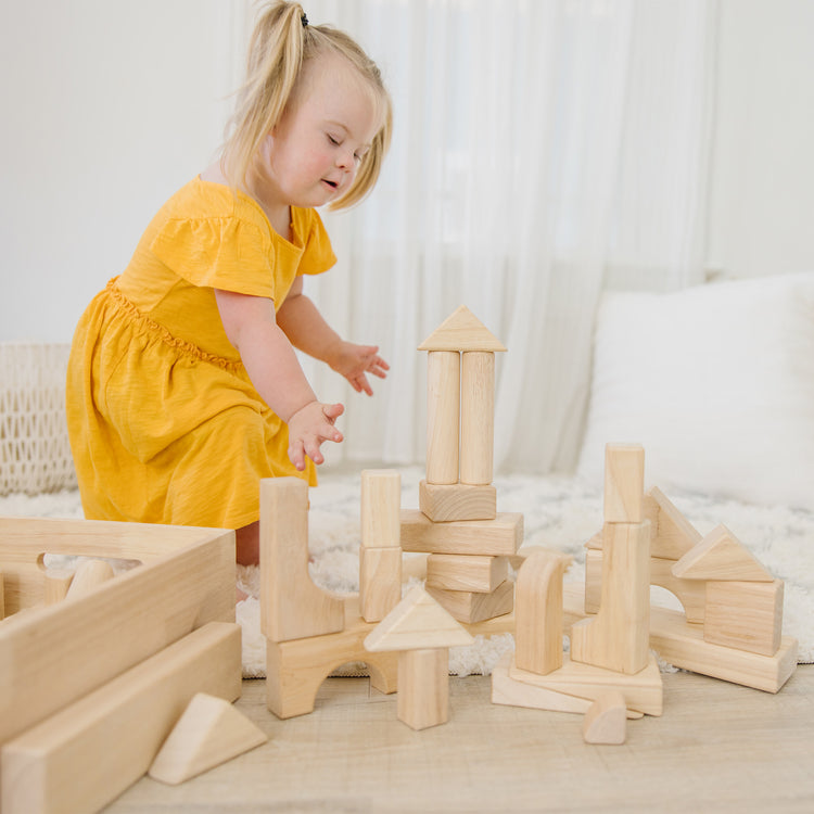 A kid playing with The Melissa & Doug Standard Unit Solid-Wood Building Blocks With Wooden Storage Tray (60 pcs)