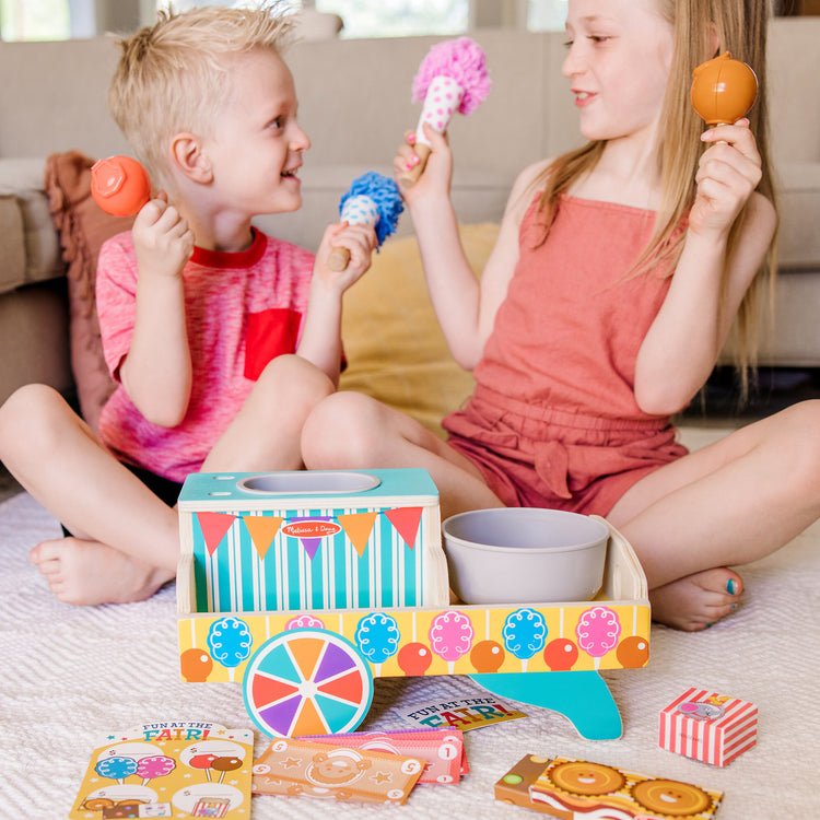 A kid playing with The Melissa & Doug Fun at the Fair! Wooden Carnival Candy Tabletop Cart and Play Food Set