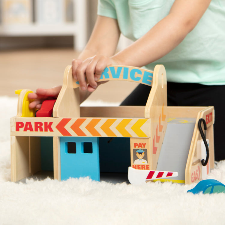 A kid playing with The Melissa & Doug Service Station Parking Garage With 2 Wooden Cars and Drive-Thru Car Wash