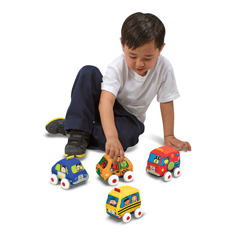 A kid playing with The Melissa & Doug K's Kids Pull-Back Vehicle Set - Soft Baby Toy Set With 4 Cars and Trucks and Carrying Case