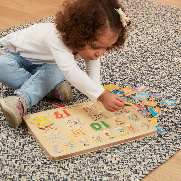 A kid playing with The Melissa & Doug Numbers Sound Puzzle - Wooden Counting Puzzle With Sound Effects (21 pcs)