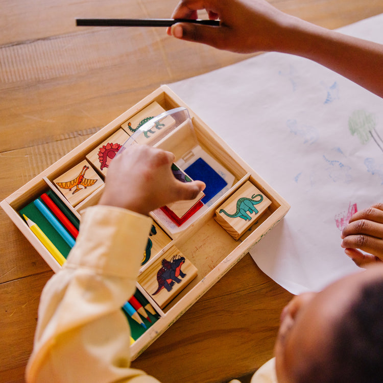 A kid playing with The Melissa & Doug Wooden Stamp Set: Dinosaurs - 8 Stamps, 5 Colored Pencils, 2-Color Stamp Pad