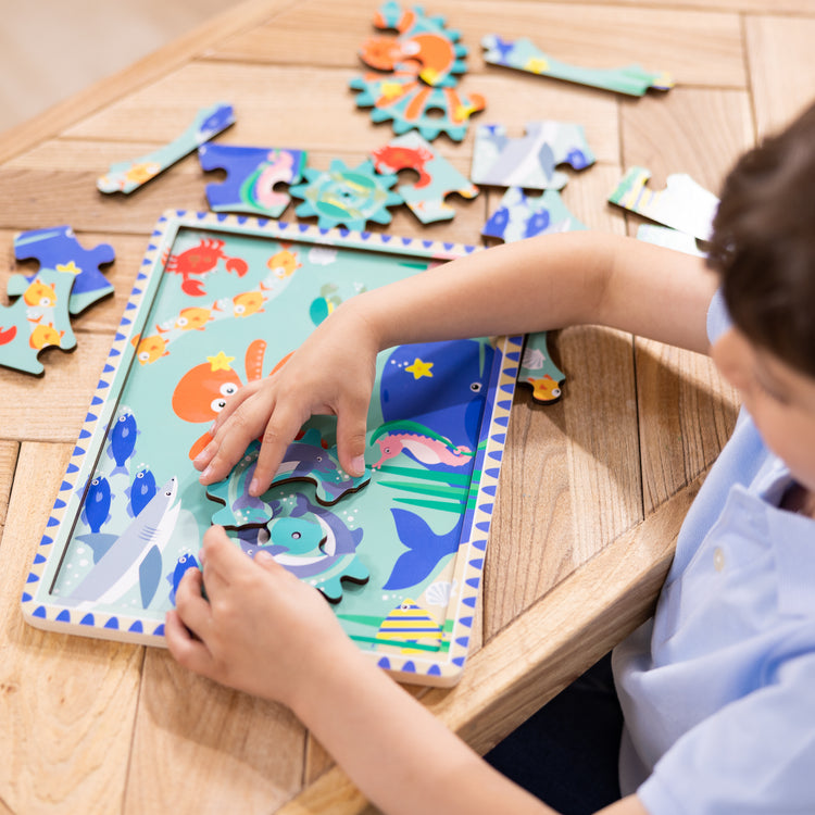 A kid playing with The Melissa & Doug Wooden Underwater Jigsaw Spinning Gear Puzzle – 18 Pieces