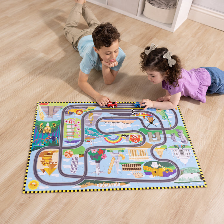 A kid playing with The Melissa & Doug Race Around the World Tracks Cardboard Jigsaw Floor Puzzle and Wind-Up Vehicles – 48 Pieces, for Boys and Girls 3+