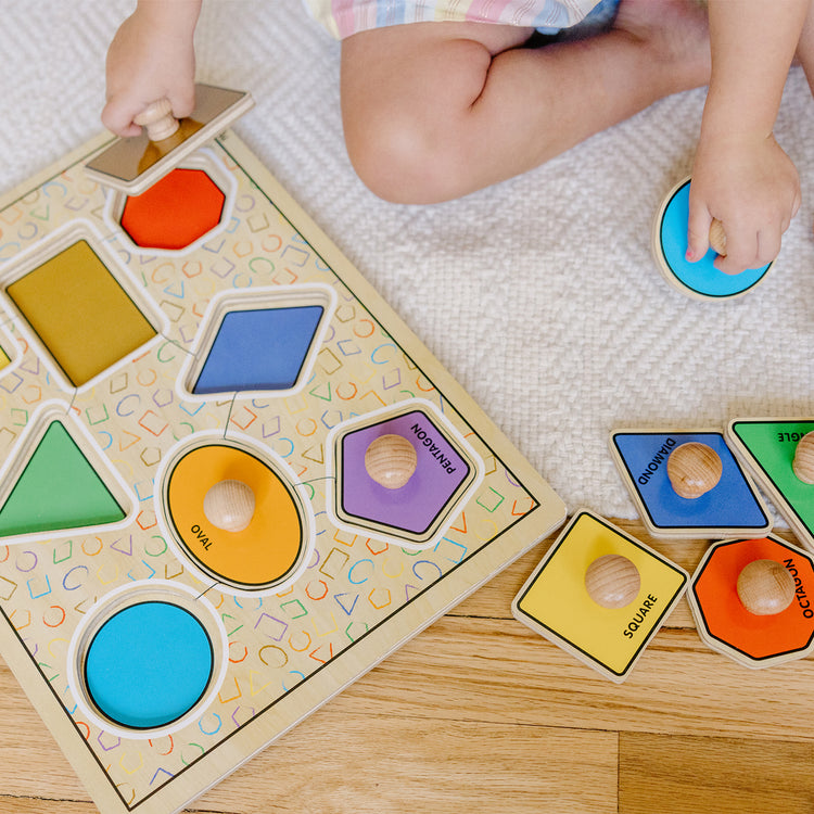 A kid playing with The Melissa & Doug Deluxe Jumbo Knob Wooden Puzzle - Geometric Shapes (8 pcs)