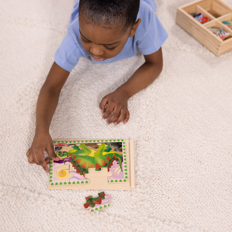 A kid playing with The Melissa & Doug Dinosaurs 4-in-1 Wooden Jigsaw Puzzles in a Storage Box (48 pcs)