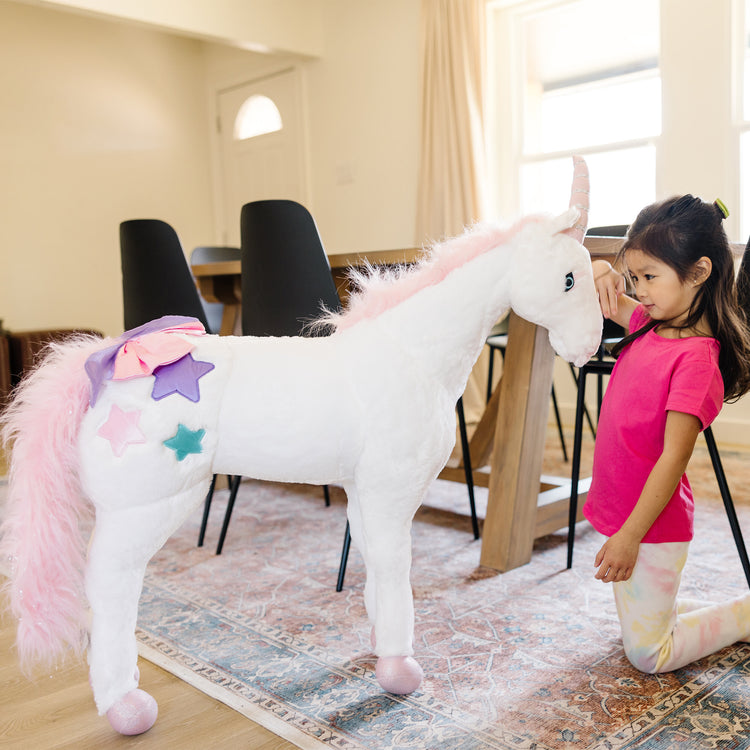 A kid playing with The Melissa & Doug Giant Unicorn - Lifelike Plush Stuffed Animal (over 2 feet tall)