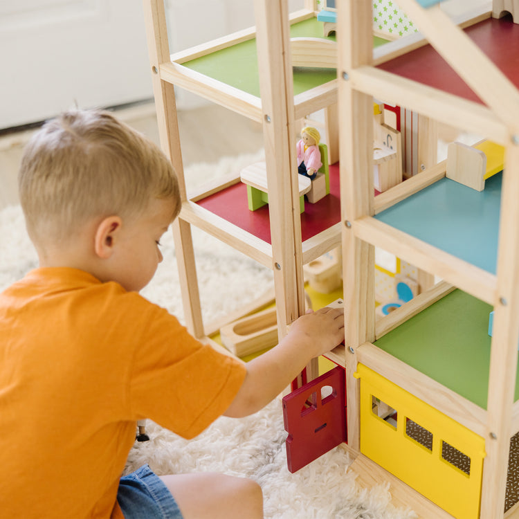 A kid playing with The Melissa & Doug Wooden Hi-Rise Dollhouse With 15 Furniture Pieces, Garage, Working Elevator