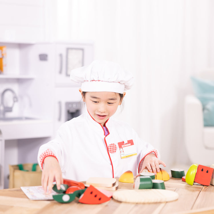 A kid playing with The Melissa & Doug Chef Role Play Costume Dress -Up Set With Realistic Accessories