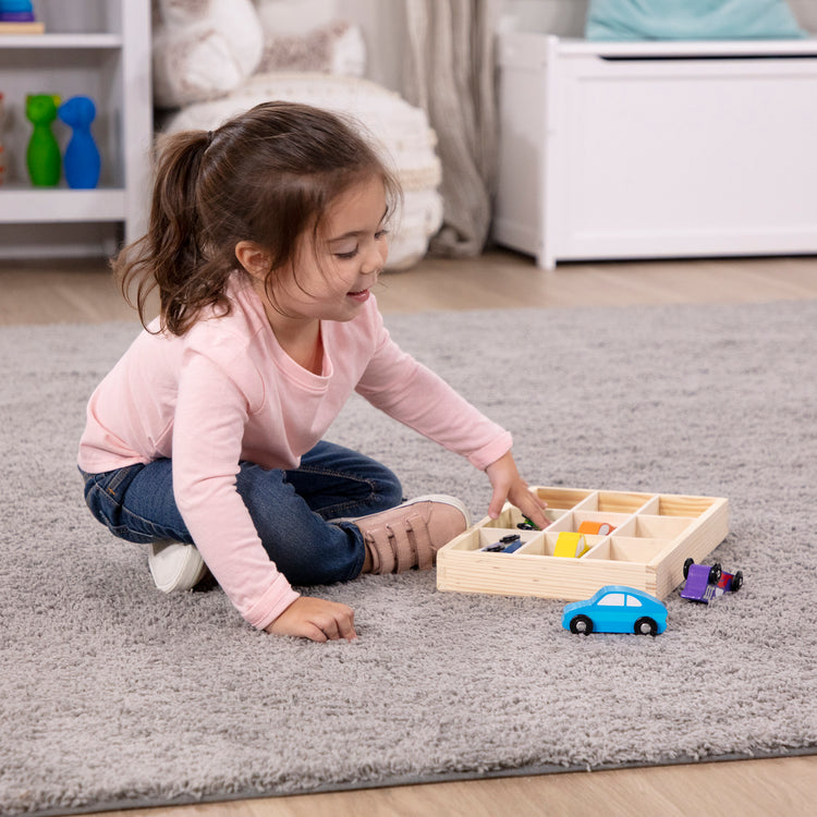 A kid playing with The Melissa & Doug Wooden Cars Vehicle Set in Wooden Tray - 9 Pieces