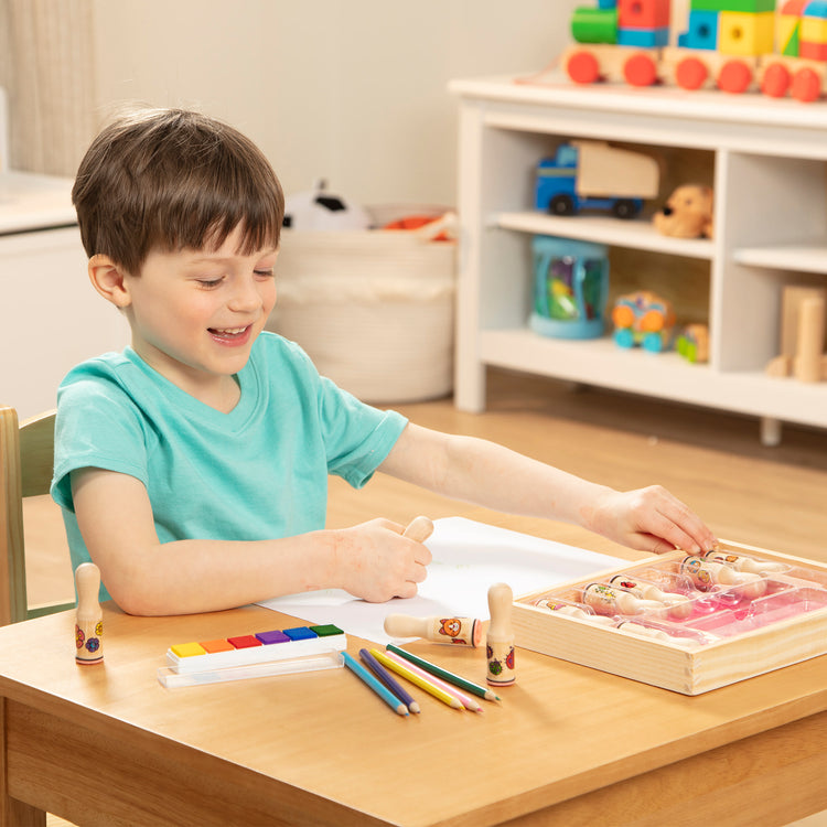 A kid playing with The Melissa & Doug Deluxe Happy Handle Stamp Set With 10 Stamps, 5 Colored Pencils, and 6-Color Washable Ink Pad