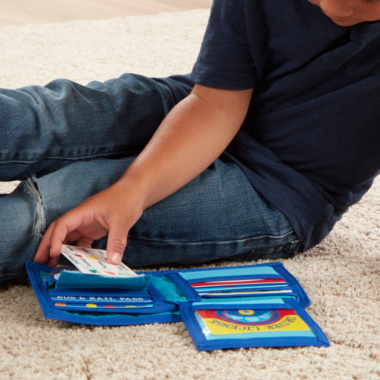 A kid playing with The Melissa & Doug Pretend-to-Spend Toy Wallet With Play Money and Cards (45 pcs), Blue