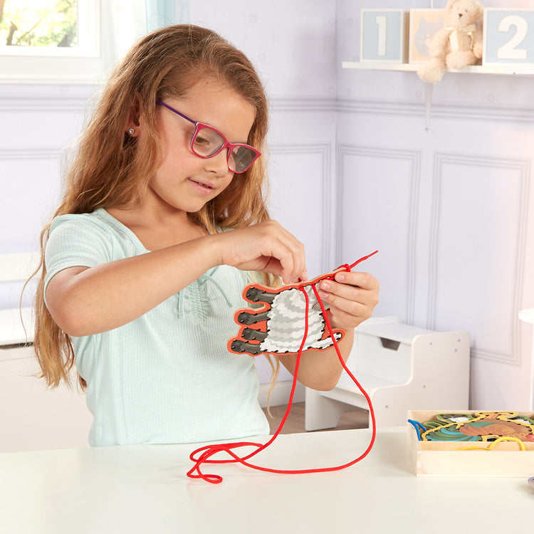 A kid playing with The Melissa & Doug Lace and Trace Activity Set: 5 Wooden Panels and 5 Matching Laces - Farm