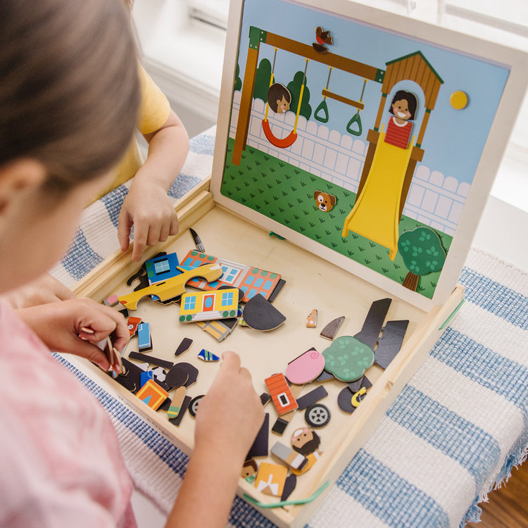 A kid playing with The Melissa & Doug Wooden Magnetic Matching Picture Game With 119 Magnets and Scene Cards