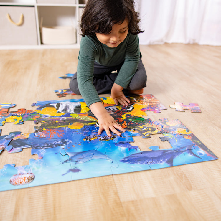 A kid playing with The Melissa & Doug Underwater Ocean Floor Puzzle (48 pcs, 2 x 3 feet)