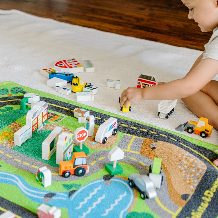 A kid playing with The Melissa & Doug Deluxe Activity Road Rug Play Set with 49 Wooden Vehicles and Play Pieces