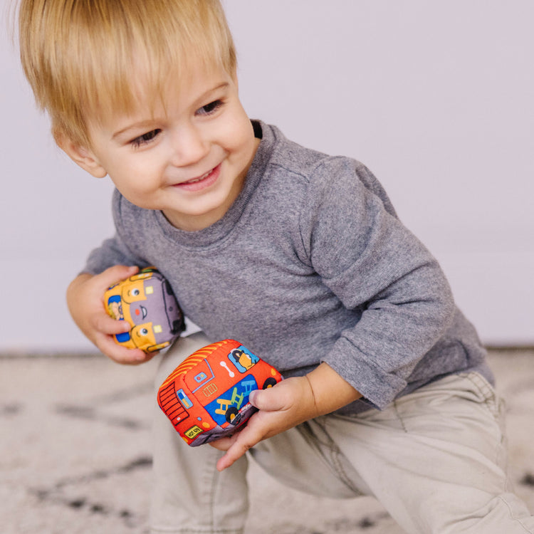 A kid playing with The Melissa & Doug Take-Along Town Play Mat (19.25 x 14.25 inches) With 9 Soft Vehicles