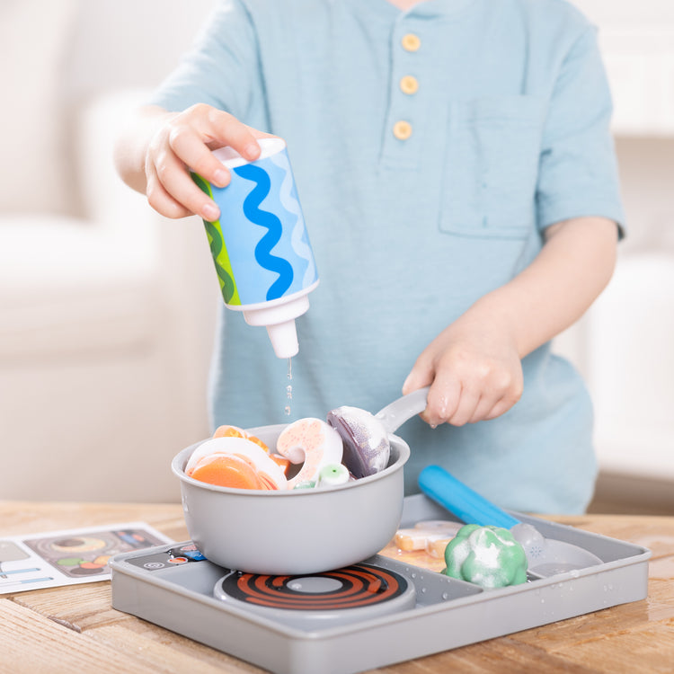 A kid playing with The Melissa & Doug Simmer & Stir Stovetop Play Set with Water WOW!® Color Reveal Play Food Preschool Toy Ages 3+