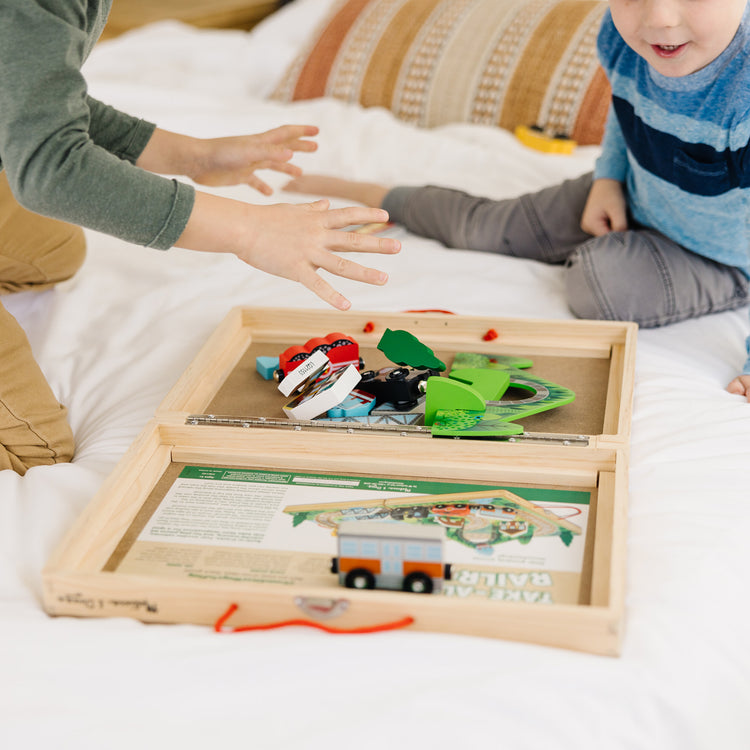 A kid playing with The Melissa & Doug 17-Piece Wooden Take-Along Tabletop Railroad, 3 Trains, Truck, Play Pieces, Bridge