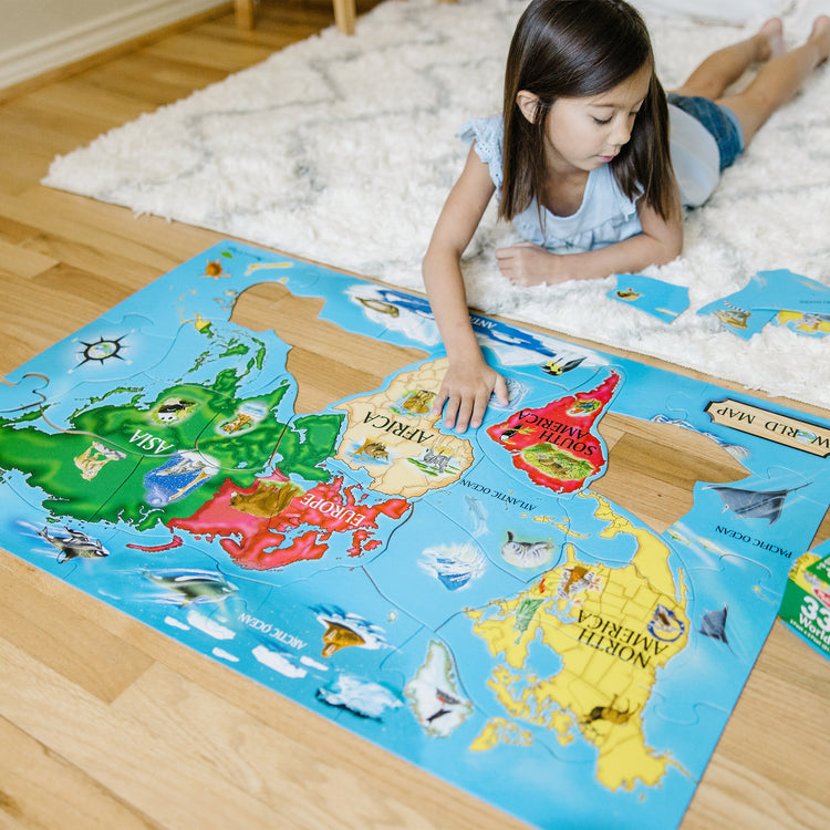 A kid playing with The Melissa & Doug World Map Jumbo Jigsaw Floor Puzzle (33 pcs, 2 x 3 feet)