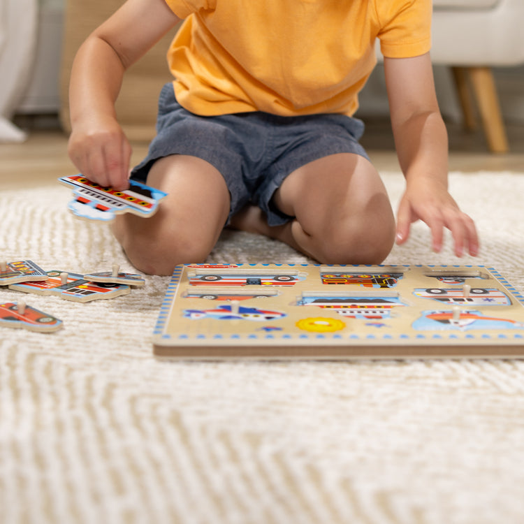 A kid playing with The Melissa & Doug Vehicles Sound Puzzle - Wooden Peg Puzzle With Sound Effects (8 pcs)