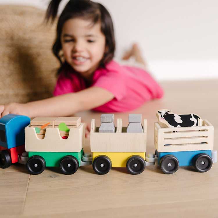 A kid playing with The Melissa & Doug Wooden Farm Train Set - Classic Wooden Toy (3 linking cars)