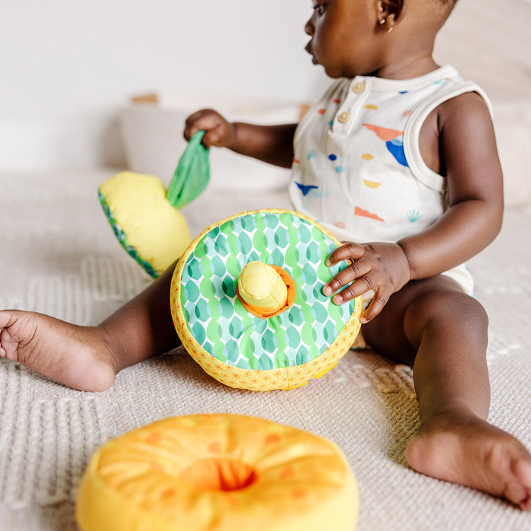 A kid playing with The Melissa & Doug Multi-Sensory Pineapple Soft Stacker Infant Toy