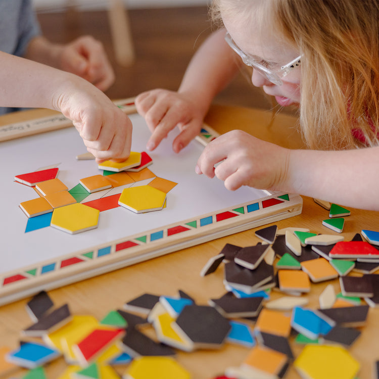 A kid playing with The Melissa & Doug Deluxe Wooden Magnetic Pattern Blocks Set - Educational Toy With 120 Magnets and Carrying Case