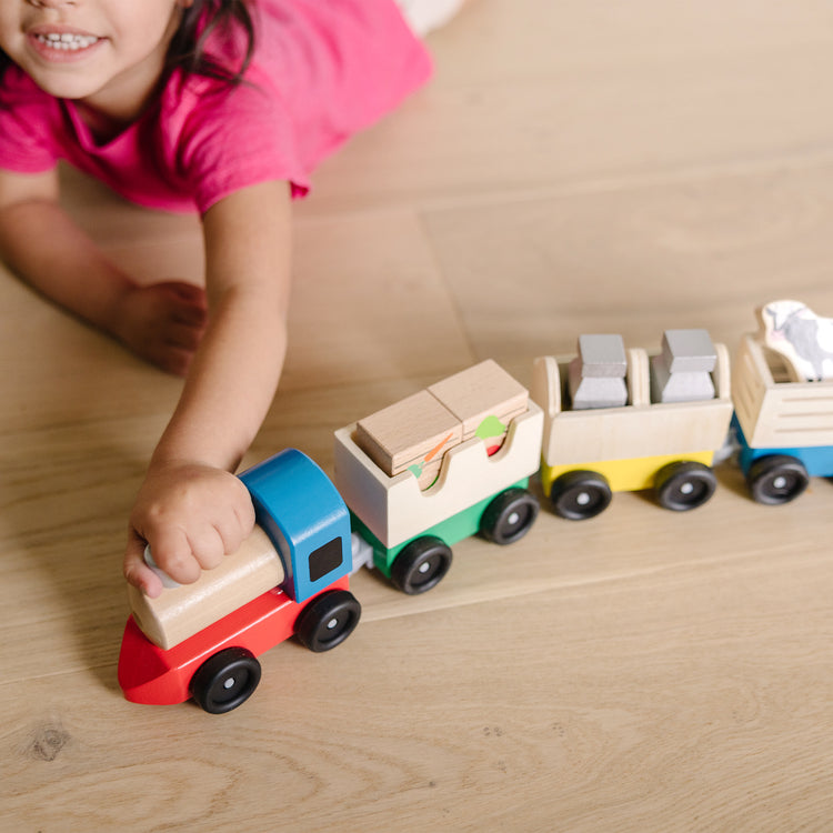 A kid playing with The Melissa & Doug Wooden Farm Train Set - Classic Wooden Toy (3 linking cars)