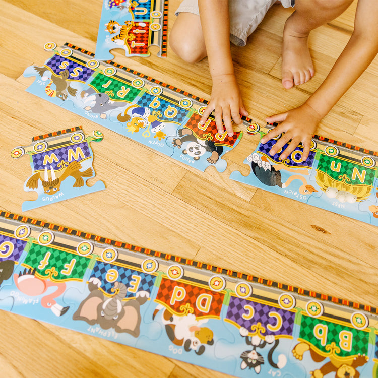 A kid playing with The Melissa & Doug Alphabet Express Jumbo Jigsaw Floor Puzzle (27 pcs, 10 feet long)