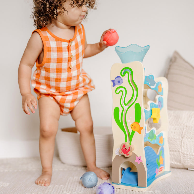 A kid playing with The Melissa & Doug Rollables Wooden Ocean Slide Infant and Toddler Toy (5 Pieces)