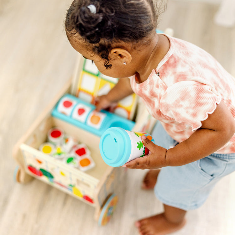 A kid playing with The Melissa & Doug Wooden Shape Sorting Grocery Cart Push Toy and Puzzles