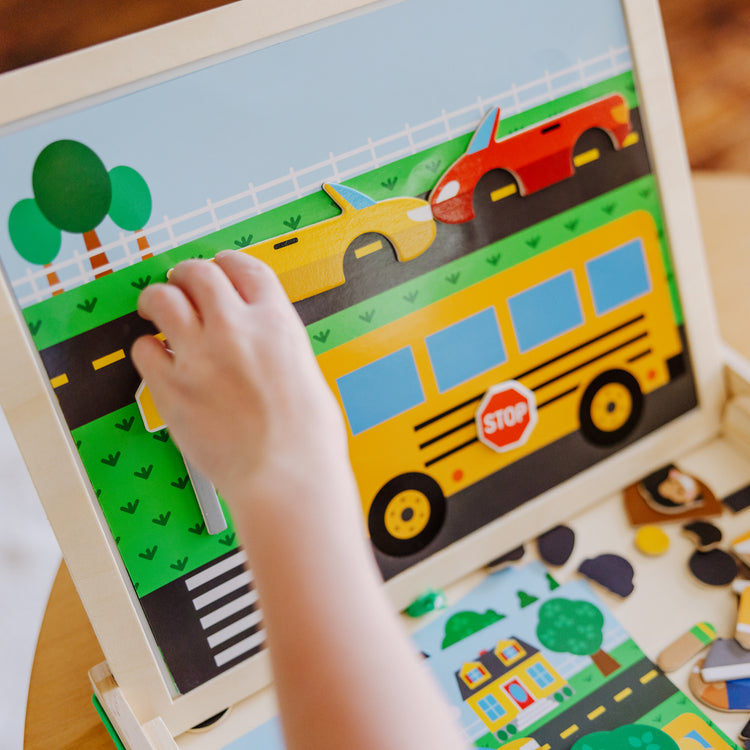 A kid playing with The Melissa & Doug Wooden Magnetic Matching Picture Game With 119 Magnets and Scene Cards