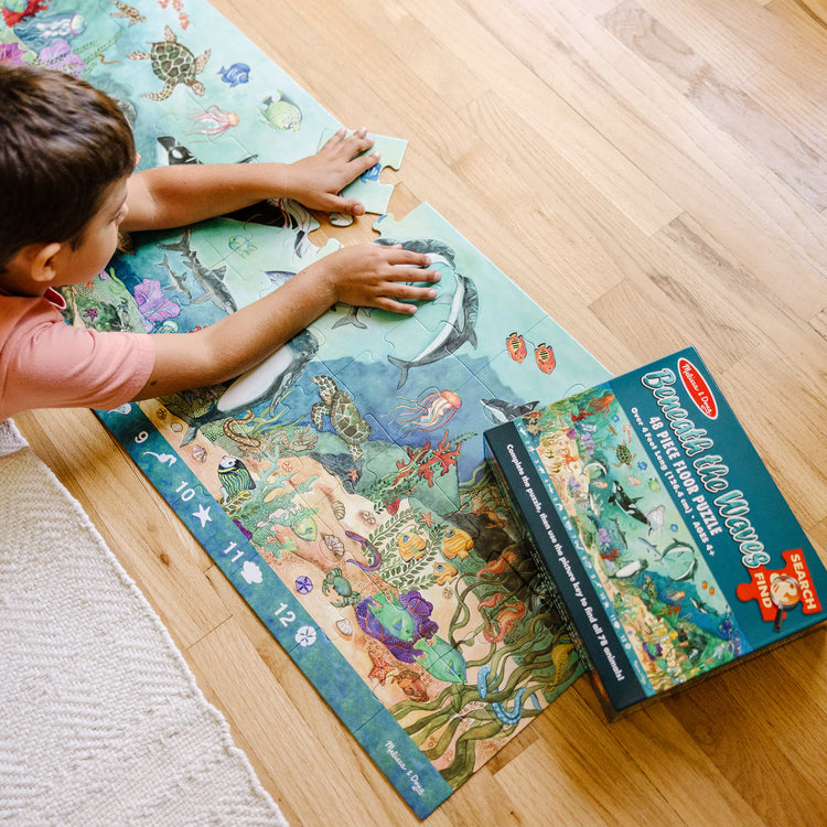 A kid playing with The Melissa & Doug Search and Find Beneath the Waves Floor Puzzle (48 pcs, over 4 feet long)