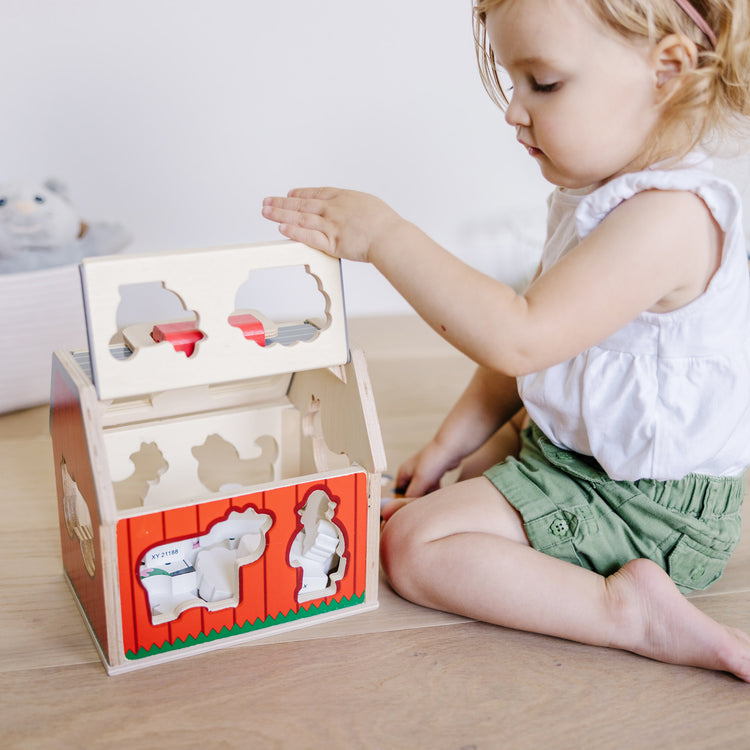 A kid playing with The Melissa & Doug Wooden Take-Along Sorting Barn Toy with Flip-Up Roof and Handle 10 Wooden Farm Play Pieces