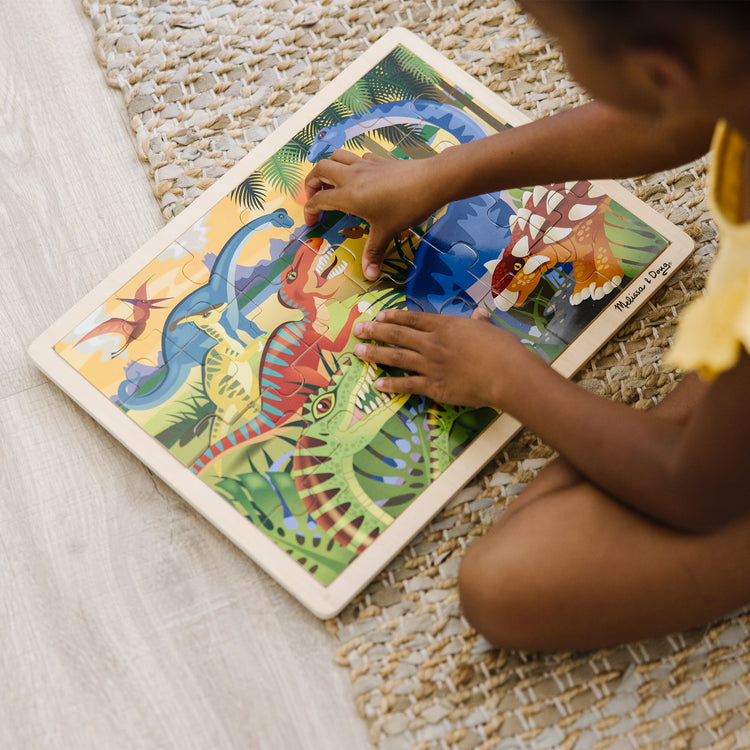 A kid playing with The Melissa & Doug Dinosaurs Wooden Jigsaw Puzzle With Storage Tray (24 pcs)