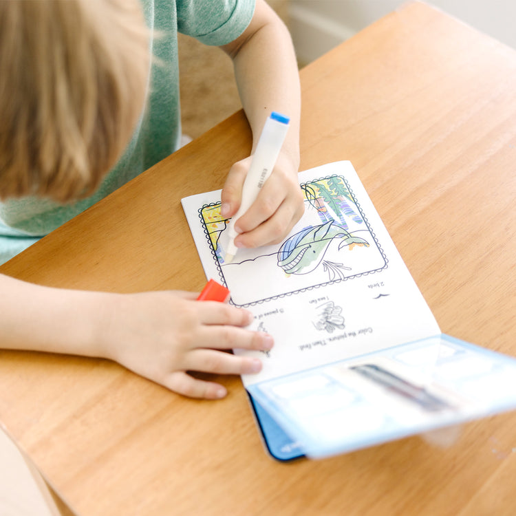 A kid playing with The Melissa & Doug On the Go ColorBlast! Activity Book: Sea Life - 24 Pictures and No-Mess Pen