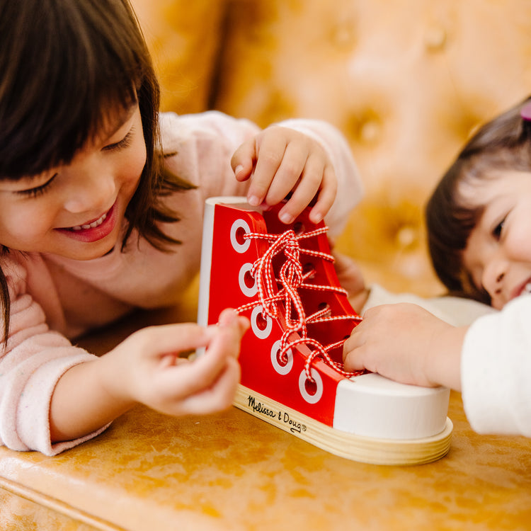 A kid playing with The Melissa & Doug Deluxe Wood Lacing Sneaker - Learn to Tie a Shoe Educational Toy