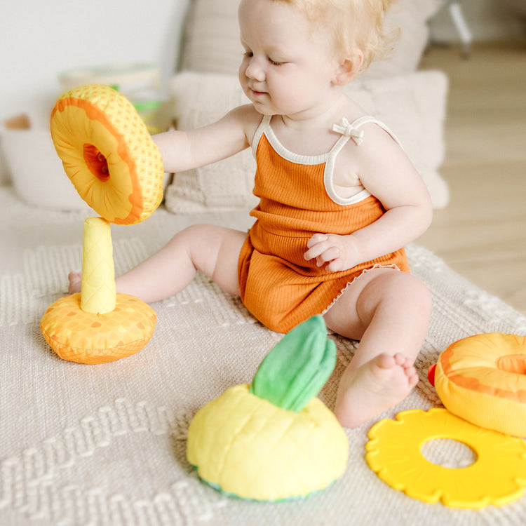 A kid playing with The Melissa & Doug Multi-Sensory Pineapple Soft Stacker Infant Toy