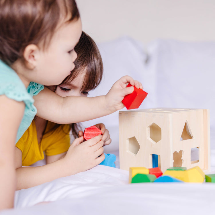 A kid playing with The Melissa & Doug Shape Sorting Cube - Classic Wooden Toy With 12 Shapes