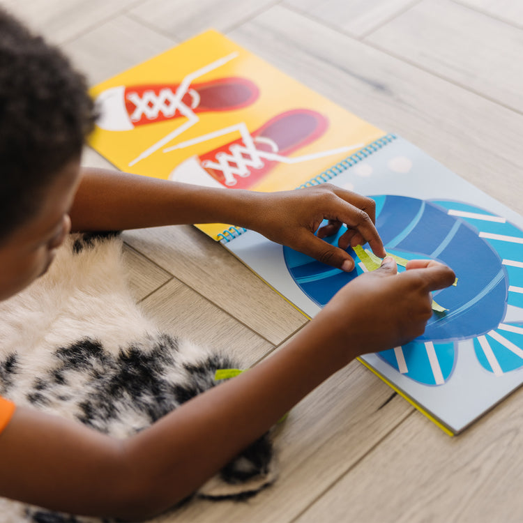 A kid playing with The Melissa & Doug Tape Activity Book: 4 Rolls of Easy-Tear Tape and 20 Reusable Scenes